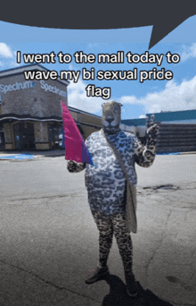 a person dressed as a leopard holding a bisexual pride flag in front of a spectrum store