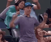 a man in a purple shirt is dancing in front of a crowd of people at a baseball game .