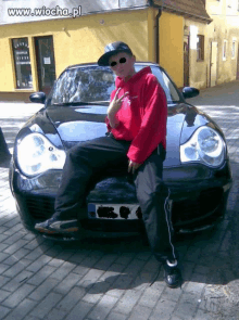 a man in a red hoodie is sitting on the hood of a black car