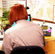 a woman with red hair is sitting at a desk with a telephone and a map on the wall behind her