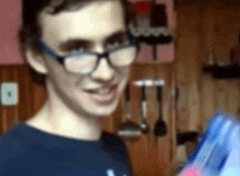 a young man wearing glasses and a blue shirt is holding a blue box .