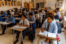 a group of students sit at desks in a classroom with a whiteboard that says ' physics ' on it