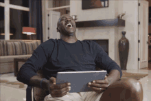 a man is laughing while holding a tablet in his hands