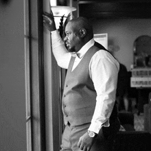 a man in a suit leans against a wall and looks out a window