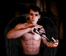 a shirtless man with black wings is holding a cross in his hands