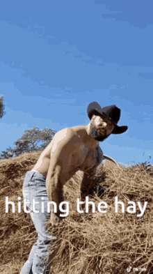 a shirtless cowboy is standing next to a pile of hay .