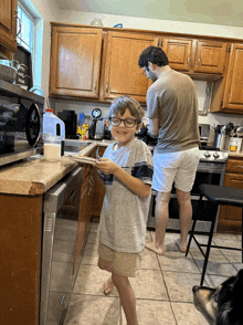 a young boy with glasses stands in a kitchen holding a plate