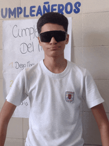 a boy wearing sunglasses is standing in front of a sign that says cumpleañeros