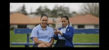 two women are sitting on a blue bench and one is using sign language .