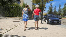 two women are walking down a sidewalk next to a car with license plate number tc - jc - 054