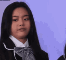 a girl in a school uniform with long black hair and a bow tie is making a funny face .