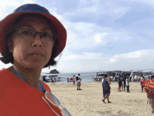 a woman wearing glasses and a red hat stands on the beach