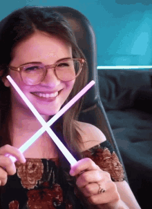 a woman wearing glasses is smiling while holding a pair of glow in the dark sticks