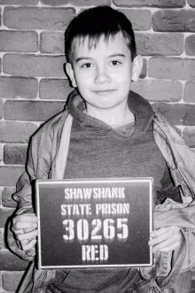 a young boy holds up a shawshank state prison 30265 red sign