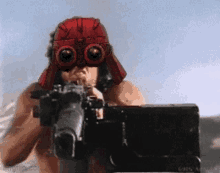 a shirtless man wearing a red helmet and goggles is holding a gun