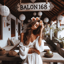 a woman in a white dress is standing in front of a sign that says balon 168