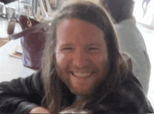 a man with long hair and a beard smiles at the camera