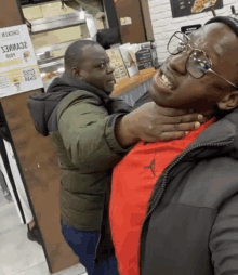 a man in a red shirt is being choked by another man in front of a sign that says chicken