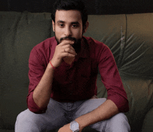 a man in a red shirt is sitting on a couch with his hand on his chin