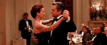 a man in a tuxedo and a woman in a dress are dancing in a room filled with people .