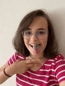 a girl wearing glasses and a pink and white striped shirt is sticking her tongue out