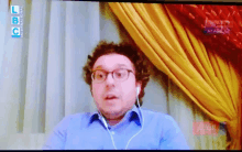 a tv screen shows a man wearing glasses and ear buds and says lbc on the top left