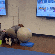 a woman squatting next to a large exercise ball in front of a tv that says ' pilates ' on it