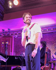 a man is holding a microphone and smiling in front of a purple background