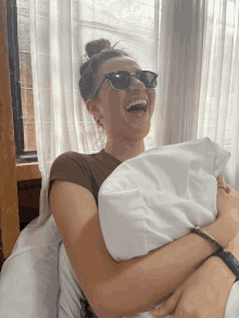 a woman wearing sunglasses is laughing and holding a white pillow