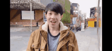 a young man in a brown jacket stands in front of a building with a sign that says ' coca cola '