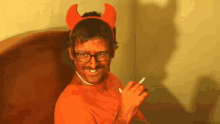 a man dressed as a devil is smoking a cigarette and wearing horns .