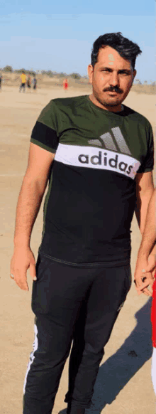 a man with a mustache is wearing a green adidas shirt