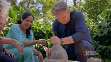 a man in a blue shirt is kneeling next to a woman in a blue dress and a national geographic logo