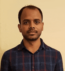 a man in a plaid shirt is standing in front of a yellow wall .