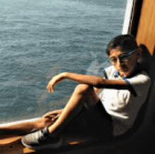 a young boy wearing glasses is sitting on a boat looking out at the water .