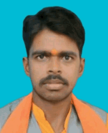 a man with an orange scarf around his neck looks at the camera with a blue background