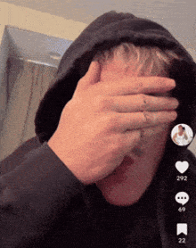 a man in a black hoodie covering his face with his hands