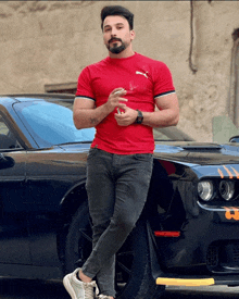 a man in a red shirt is leaning on a black car