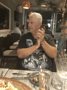 a man wearing a black shirt with a wolf on it sits at a table in a restaurant