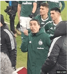 a man in a green jacket is standing on a soccer field with a group of players .