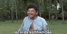 a man in a blue shirt is laughing in a field with the words `` records koltham laa '' above him .