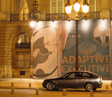 a car is parked in front of a billboard that says " the adaptive executive "