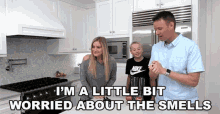 a man and a woman are standing in a kitchen with a boy . the man is wearing a nike shirt .