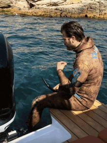 a man wearing a wet suit with the word shark on the back sits on the edge of a boat