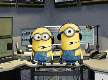 two minions wearing headphones are standing next to each other on a desk in an office .