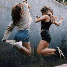 two women are jumping in the air in front of a blue wall .