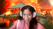 a woman wearing headphones is standing in front of a house on fire .