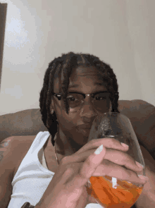 a young man wearing glasses is holding a glass of orange liquid