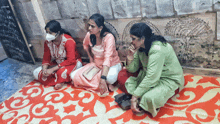 three women are sitting on a rug with one wearing a face mask