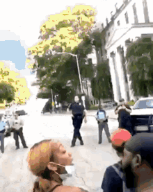 a group of people are standing on a street in front of a building . one of the people is wearing a mask .